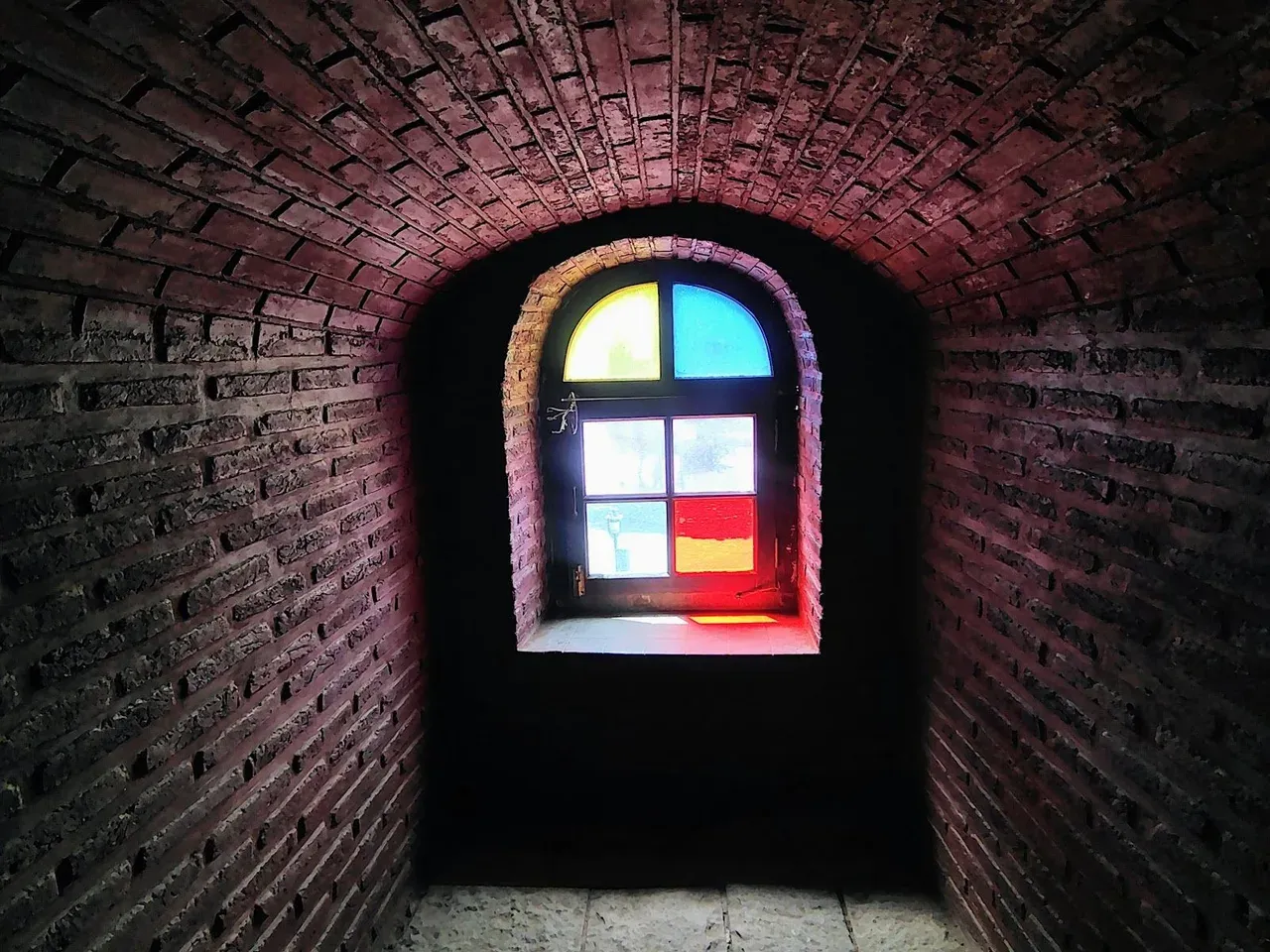 Stained glass window at the end of a brick tunnel